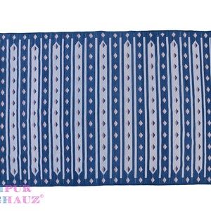 May include: A blue and white striped rug with pink accents. The rug has a geometric pattern and is made of cotton. The rug is fringed on all sides. "JAIPUR RUGHAUZ" is printed in pink on the bottom right corner.