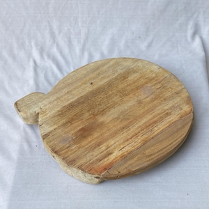 以下が含まれることがあります： ハンドル付きの丸い木製まな板。 まな板は、木目がはっきりと見える、自然な仕上がりの明るい茶色の木材で作られています。 ハンドルは長方形で、まな板の側面から伸びています。