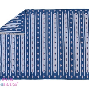 May include: A blue and white striped rug with a geometric pattern. The rug has pink accents and fringe on all sides. The rug is made of cotton and is perfect for adding a touch of bohemian style to any room.