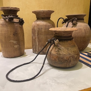 Puede incluir: Cuatro recipientes de madera con asas de cuerda. Los recipientes son marrones y tienen un aspecto rústico. Están dispuestos sobre una superficie blanca.