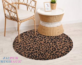 May include: A round brown and black leopard print rug with a woven texture. The rug is on a light wood floor next to a wicker chair and a small wicker table with a white top.