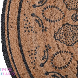 May include: A round jute rug with a black and white geometric pattern. The rug has a black border and is made of natural fibers.