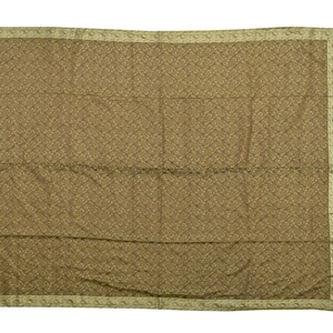 May include: A large, rectangular, olive-green textile with a repeating geometric pattern. The edges are bordered with a lighter, patterned trim. The fabric appears to be soft and draped, suggesting a scarf, shawl, or decorative cloth.