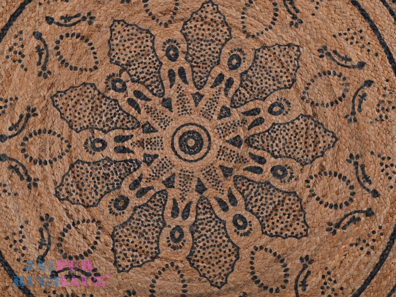 May include: A brown woven rug with a black and white geometric design. The design features a central circle with radiating lines and dots.