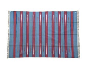 May include: A rectangular textile with a blue background and vertical red stripes. White, elongated teardrop shapes are centered within the red stripes. The edges have a fringe.