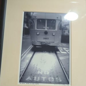 May include: Black and white framed photograph of a streetcar on tracks, with the number 1063 visible on the front. The street reads "NO AUTOS". The photograph is signed and dated "Dec 2006".