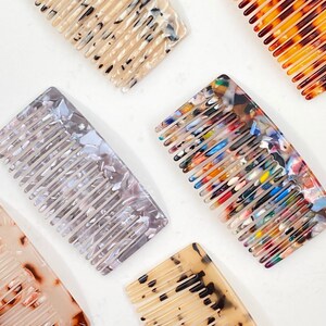 May include: Five different combs with a tortoiseshell pattern. The combs are made of plastic and have a variety of colors, including brown, black, white, blue, red, and yellow.