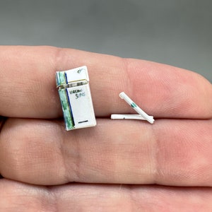 May include: A pack of Virginia Slims cigarettes with a green and white design. The pack is open and two cigarettes are sticking out.