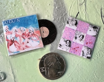 Puede incluir: Un conjunto de tres discos de vinilo vintage, que incluye un disco de Go-Go's, un disco de vinilo negro y un disco con un patrón de cuadros y imágenes en blanco y negro de personas.
