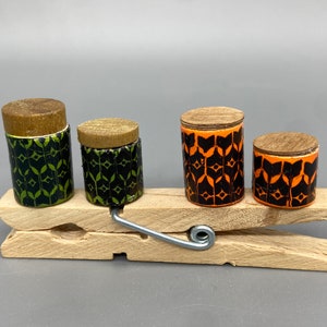 May include: Four small decorative containers with black and white floral patterns on a wooden clothespin. Two containers are orange and two are green.