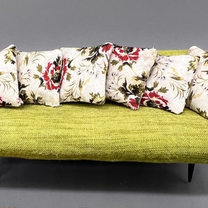Puede incluir: Un sof&aacute; de tela verde con seis almohadas con estampado floral. El sof&aacute; tiene brazos de madera y patas negras.