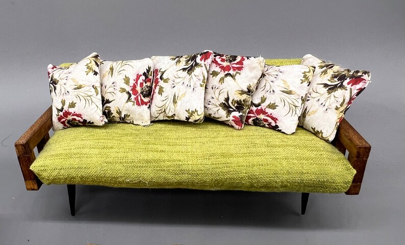 Puede incluir: Un sof&aacute; de tela verde con seis almohadas con estampado floral. El sof&aacute; tiene brazos de madera y patas negras.