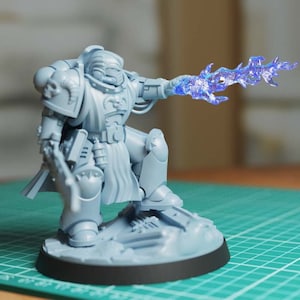 May include: A gray plastic miniature of a space marine holding a blue energy weapon. The miniature is posed in a dynamic action pose and is standing on a gray plastic base.