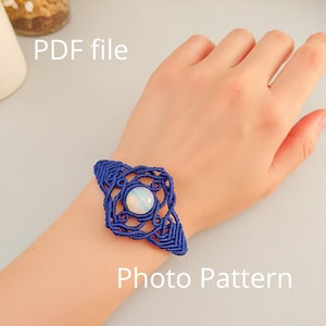 Puede incluir: Un brazalete de macramé azul con una piedra blanca central se muestra en una muñeca. El brazalete tiene un diseño intrincado. El texto "PDF file" y "Photo Pattern" son visibles en la imagen.