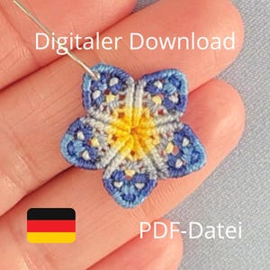 May include: A crocheted flower in blue, yellow, and white, held with a needle. The flower has five petals. The image includes the text "Digitaler Download" and "PDF-Datei". A German flag is also in the image.