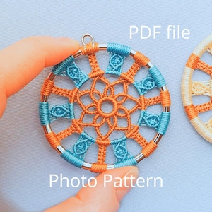 May include: A close-up of a small, round, orange and blue macrame dreamcatcher with a silver metal ring. The dreamcatcher is hanging from a silver loop. The text "PDF file" and "Photo Pattern" are visible in the image.