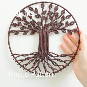 May include: A brown macrame wall hanging in the shape of a tree with intricate branches and roots. The tree is made with brown cord and is displayed on a white wall.