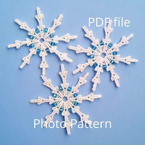 Puede incluir: Tres copos de nieve de crochet blanco con cuentas azules en el centro. Los copos de nieve están sobre un fondo azul claro. El texto "PDF file" está por encima de los copos de nieve y el texto "Photo Pattern" está por debajo de los copos de nieve.