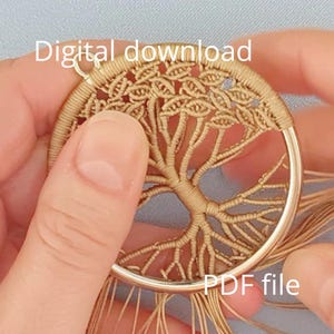 Könnte beinhalten: Ein kreisförmiger Makramee-Wandbehang mit einem Baummotiv aus beigefarbener Kordel in einem goldfarbenen Metallring. Das Stück hat oben eine kleine Schlaufe zum Aufhängen und lose Kordelstränge am unteren Ende. Text Digital download PDF file.