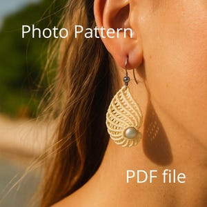 以下が含まれることがあります： クリーム色の涙型のイヤリングで、下部に真珠のようなビーズが付いています。 イヤリングは織り込まれた素材でできており、銀色のフックから吊り下げられています。 「Photo Pattern」と「PDF file」の文字が見えます。