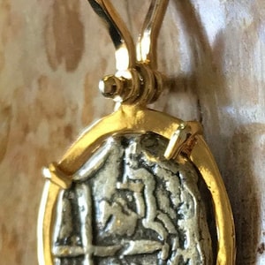 May include: A gold pendant featuring a silver coin with a cross and other markings. The coin is set in a gold frame with a bail loop.