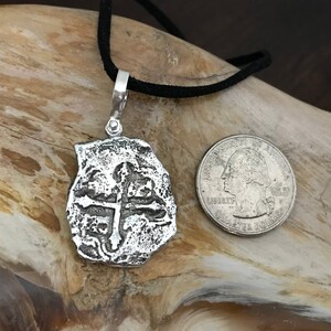 Puede incluir: Collar con colgante de plata que representa una r&eacute;plica de una moneda espa&ntilde;ola de ocho reales con un dise&ntilde;o de cruz. El colgante es aproximadamente del tama&ntilde;o de una moneda de 25 c&eacute;ntimos de euro.