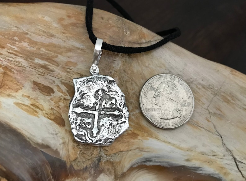 Puede incluir: Collar con colgante de plata que representa una r&eacute;plica de una moneda espa&ntilde;ola de ocho reales con un dise&ntilde;o de cruz. El colgante es aproximadamente del tama&ntilde;o de una moneda de 25 c&eacute;ntimos de euro.