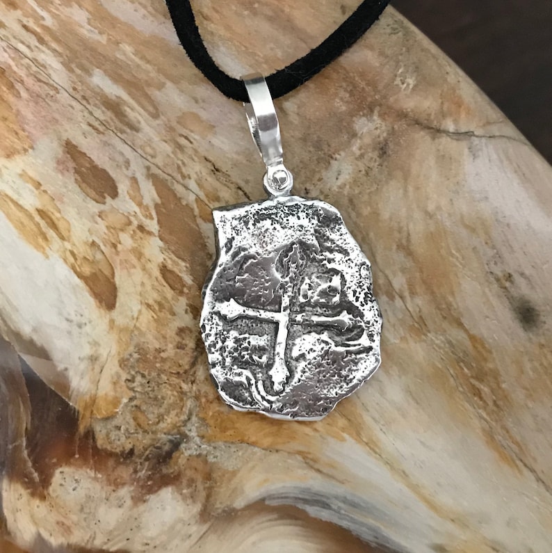 Puede incluir: Collar con colgante de plata con dise&ntilde;o de cruz. El colgante es texturizado y tiene un aspecto r&uacute;stico. El collar est&aacute; en un cord&oacute;n negro.