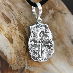 Puede incluir: Pendiente de plata con un dise&ntilde;o de cruz, que recuerda a una moneda antigua. El pendiente tiene una superficie texturizada y un aro para sujetar una cadena.