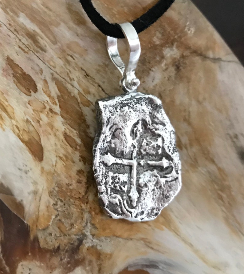 Puede incluir: Pendiente de plata con un dise&ntilde;o de cruz, que recuerda a una moneda antigua. El pendiente tiene una superficie texturizada y un aro para sujetar una cadena.
