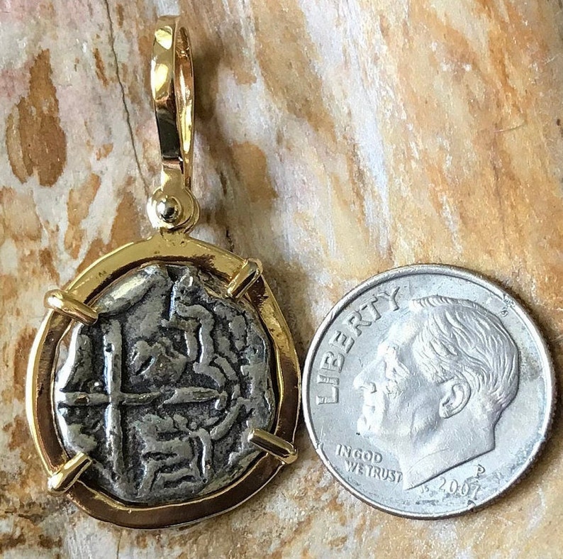 May include: A silver coin pendant with a gold frame and a cross design. The coin is about the size of a UK ten pence piece.
