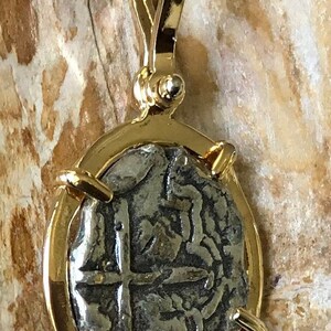 May include: A silver coin pendant with a gold frame and bail. The coin features a cross and other markings.