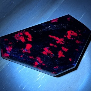 May include: A dark blue and red gemstone with a unique, irregular shape. The gemstone has a speckled appearance with red flecks throughout.
