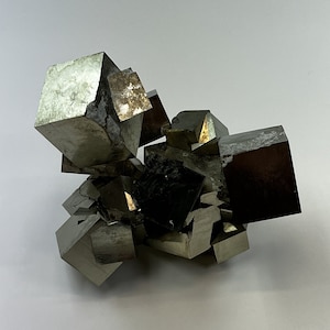 Könnte beinhalten: Ein Cluster aus Pyritkristallen, auch bekannt als Katzengold, mit einem metallischen, goldähnlichen Glanz. Die Kristalle sind in einer zufälligen, natürlichen Formation angeordnet.