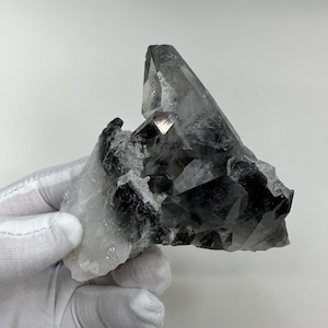 May include: A large, clear quartz crystal with black inclusions. The crystal is pointed at the top and has a rough, natural texture.