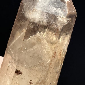 May include: A clear quartz crystal with a light brown hue and inclusions. The crystal is faceted and has a pointed tip.