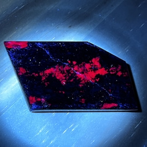 Peut inclure: Une pierre précieuse bleu foncé et rouge de forme irrégulière et brute. La pierre précieuse a un aspect moucheté avec des taches rouges partout.