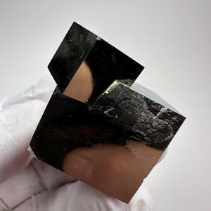 以下が含まれることがあります： 鏡のように反射する表面を持つ、独特の立方体結晶構造を特徴とする金属質の黄鉄鉱の鉱物標本。この鉱物は鋭い幾何学的なエッジと、周囲を映し出す暗く光沢のある仕上げが施されています。