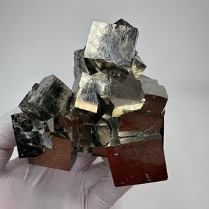 Może przedstawiać: Skupisko metalicznych kryształów pirytu z wieloma sześciennymi formacjami o odblaskowych, mosiężno-złotych powierzchniach. Okaz minerału wykazuje ostre, geometryczne krawędzie oraz złożoną, wielościenną strukturę z różnorodnymi refleksami świetlnymi.