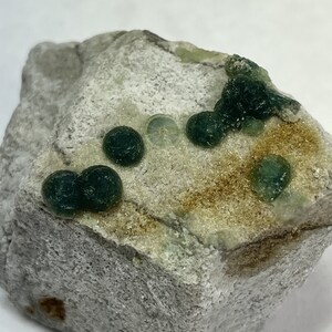 Pode incluir: Um close-up de uma rocha cinza com formações minerais redondas verdes. A rocha tem uma superfície áspera e texturizada.