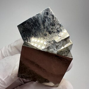 May include: A close-up of a pyrite crystal formation. The mineral has a metallic luster and a cubic structure. The top cube is slightly rotated, revealing the crystal's facets and texture. The color is a mix of gold and silver.