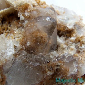 May include: A cluster of clear quartz crystals with a large, clear, faceted quartz crystal in the centre. The quartz crystals are embedded in a matrix of brown and tan rock.
