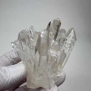 Pode incluir: Um aglomerado de cristais de quartzo transparentes e translúcidos com terminações afiadas e pontiagudas. O espécime mineral apresenta múltiplas pontas prismáticas verticais que irradiam de uma base central, exibindo facetas naturais.