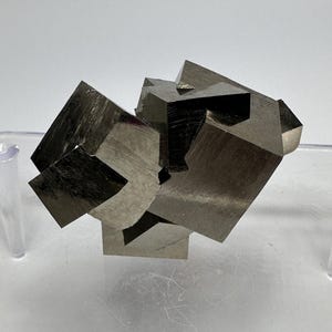 Op de afbeelding: Een cluster van pyrietkristallen, ook wel kattengoud genoemd, met een metallic zilvergrijze kleur en een kubische vorm. De kristallen zijn vergroeid en hebben een ruw, getextureerd oppervlak.