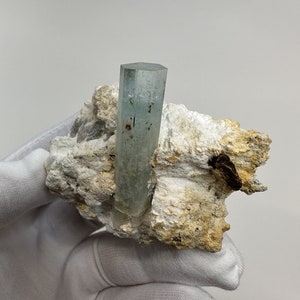 以下が含まれることがあります： 白と茶色の岩石の母岩に埋め込まれた、薄い青色のアクアマリンの結晶標本