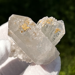 Pode incluir: Um aglomerado de cristal de quartzo transparente com inclusões douradas. O cristal é duplamente terminado e tem uma aparência natural e bruta.