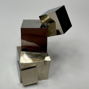 May include: A cluster of natural pyrite crystals featuring multiple interconnected metallic gold-colored cubes with sharp edges and reflective surfaces. The mineral specimen displays a geometric arrangement with distinct cubic formations and smooth faces.