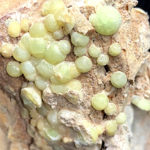 May include: A close-up of a rock formation with a cluster of small, light green, rounded crystals. The crystals are clustered together and appear to be growing out of the rock.