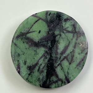 May include: A round green, black, and purple gemstone cabochon with a swirling pattern.