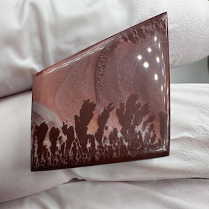 May include: A polished, trapezoidal-shaped stone cabochon featuring a smooth, glossy surface. The stone displays a muted mauve and dusty rose color palette with dark brown, tree-like dendritic inclusions spreading across the lower section.